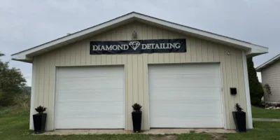 Exterior view of the Diamond Detailing storage building, featuring a light-colored metal exterior, two white garage doors, and a black business sign centered above.